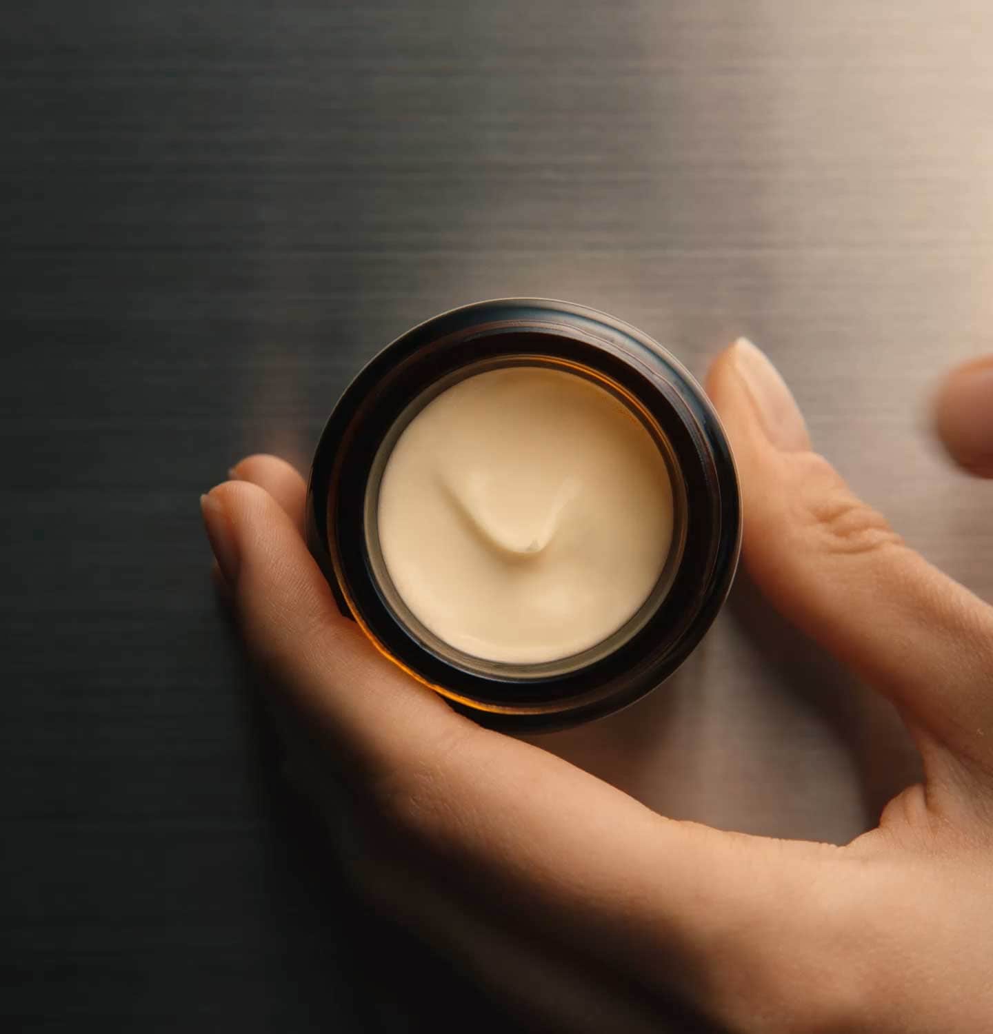 Hand holding an amber glass jar full of Camellia nut facial hydrating cream